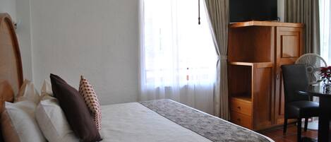 A hotel room with a bed, a desk, a chair, a television, and curtains.