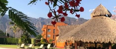 A resort with a pool, thatched-roof structures, and a mountain backdrop.