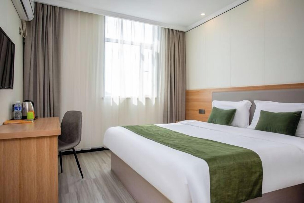 Una habitación de hotel con cama, escritorio, silla y ventana con cortinas.