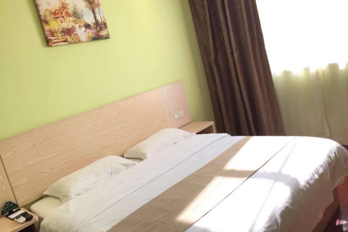 Una habitación de hotel con cama, mesita de noche, un cuadro en la pared y una ventana con cortinas.