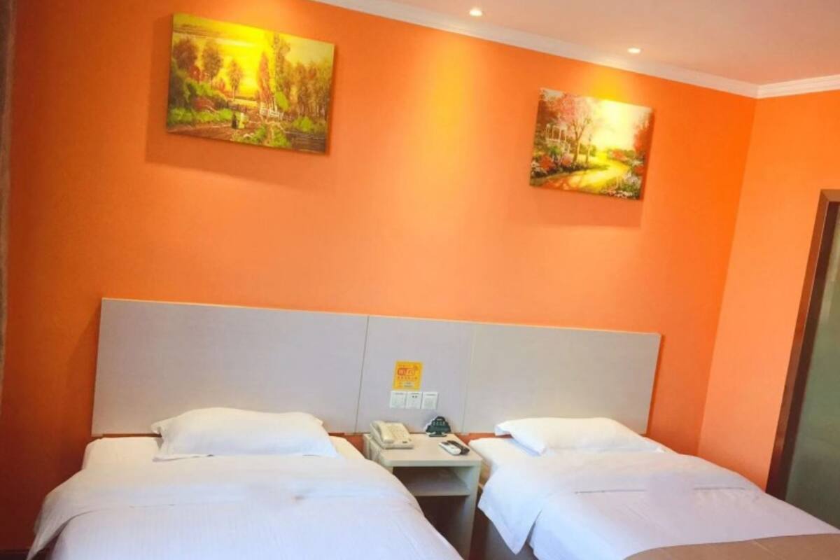 Habitación de hotel con dos camas, cabecero blanco y dos cuadros en paredes anaranjadas.