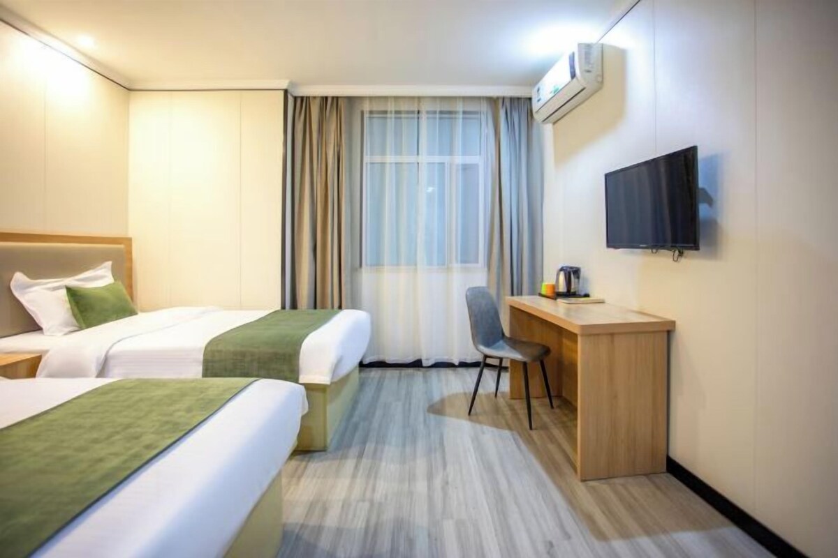 Habitación de hotel con dos camas, un escritorio, una silla, un televisor y una ventana con cortinas.