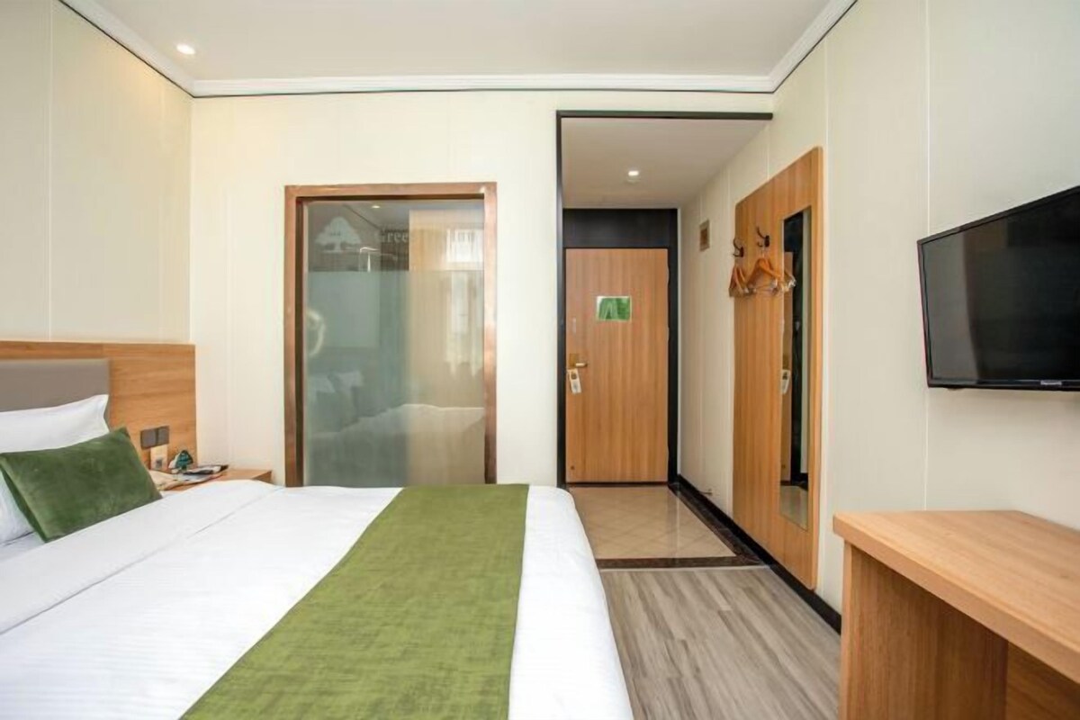 Habitación de hotel con cama, televisión, armario de madera y puerta que da a un baño.