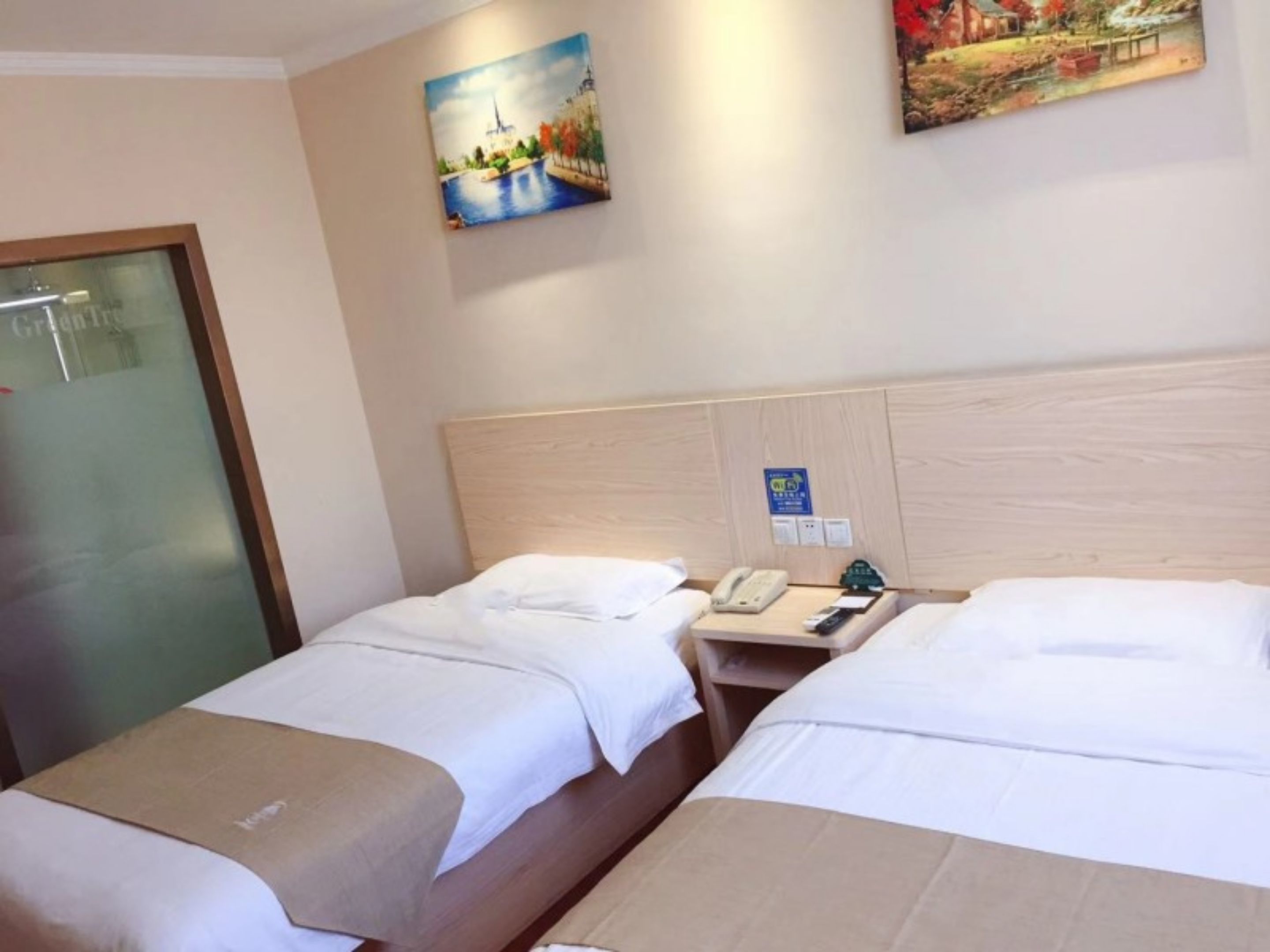 Ein Hotelzimmer mit zwei Betten, einem Holzkopfende, einem Nachttisch mit Telefon und einem Bild an der Wand.