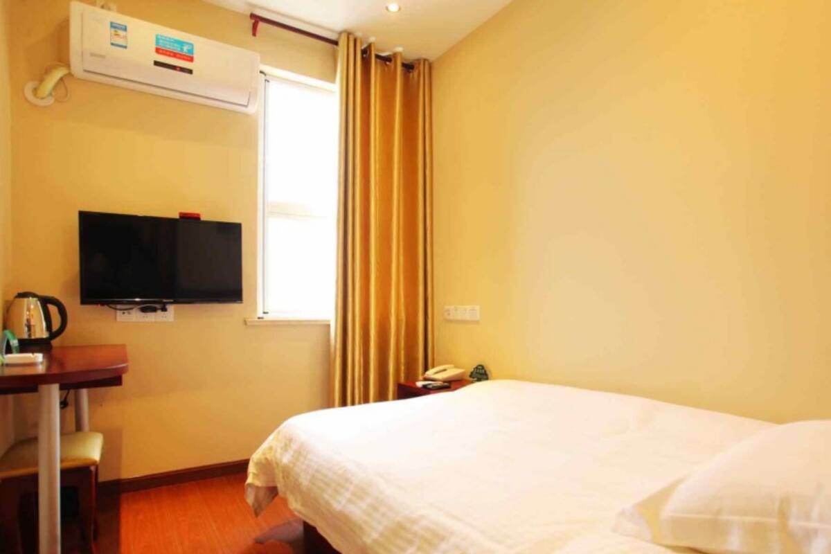 Ein Hotelzimmer mit einem Bett, einem Schreibtisch mit Fernseher, einem Fenster mit Vorhängen und einer Klimaanlage.