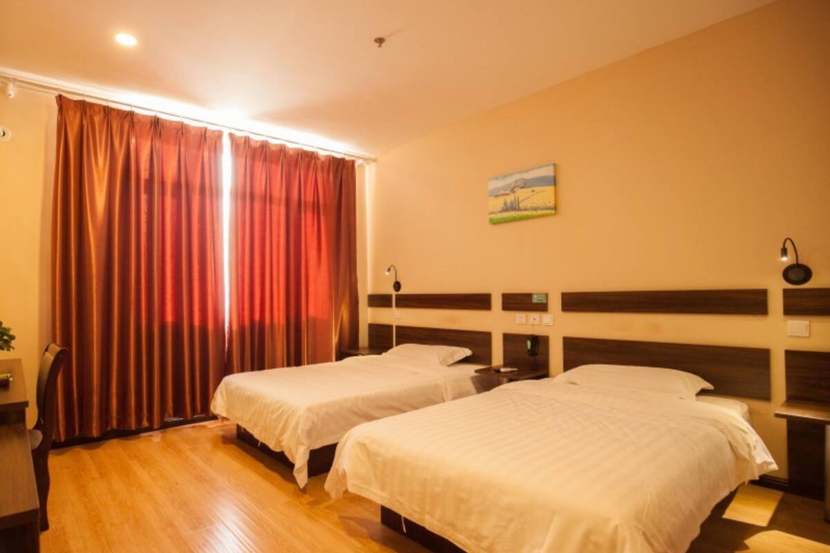 A hotel room with two single beds, wooden flooring, a painting on the wall, and a window with curtains.