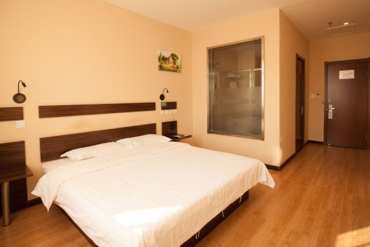 A hotel room with a large bed, wooden headboard, bedside tables, a window with a view, and a door.