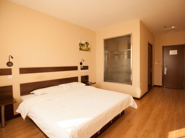Een hotelkamer met een groot bed, een houten hoofdeinde, nachtkastjes, een raam met uitzicht en een deur.