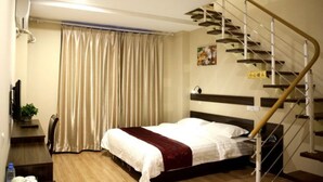 A bedroom with a bed, a desk with a chair, a potted plant, a staircase, and a painting on the wall. - GreenTree Inn DaLian Ganjingzi District Airport New District Lazishan Express Hotel (Dalian)