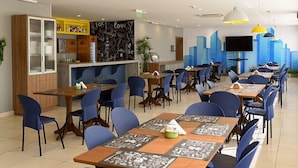 Un restaurante con varias mesas y sillas, una barra con un letrero amarillo y una pared con un menú en una pizarra.