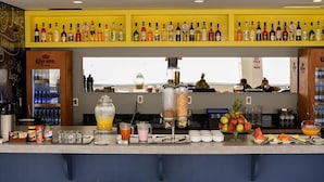 Una zona de bar con una variedad de botellas de licor, un refrigerador de Corona Extra y una exhibición de frutas.