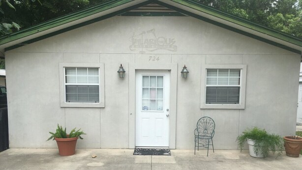 A single-story building with a white door, two windows on either side, and a small porch area with potted plants.