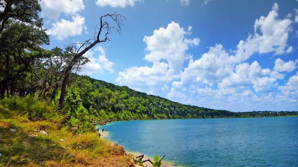 A coastal landscape with a clear sky, a calm sea, and a forested hillside. - Scriv's Haus (Winters)