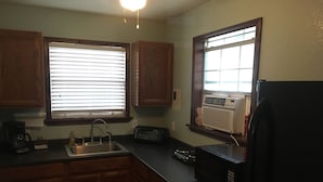 A kitchen with wooden cabinets, a sink, a microwave, and an air conditioning unit. - Scriv's Haus (Winters)