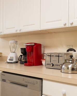 Una cocina con gabinetes blancos, una licuadora, una cafetera roja, un tostador y un hervidor.