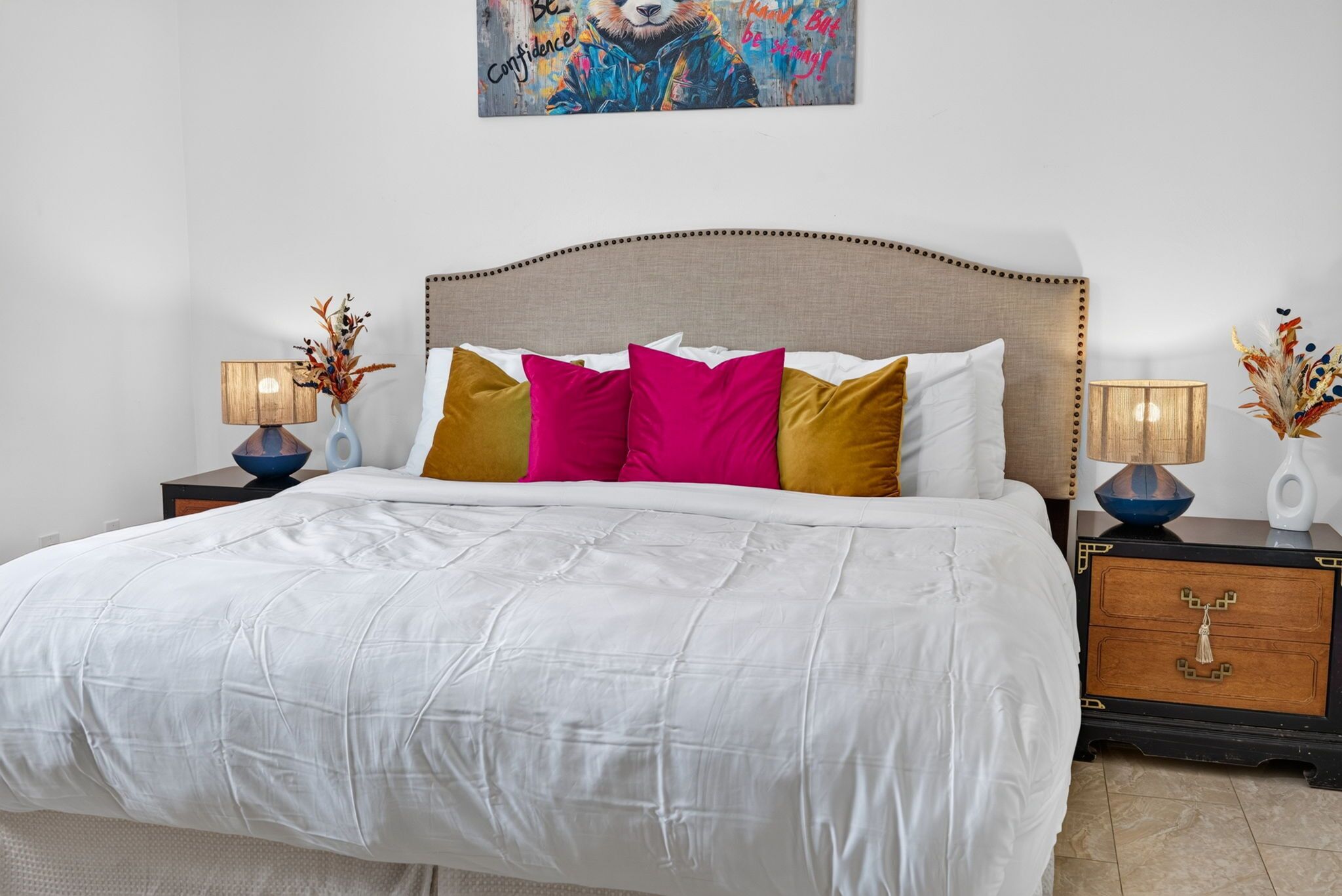 A neatly made bed with white bedding, a wooden headboard, and decorative pillows in pink and mustard colors.