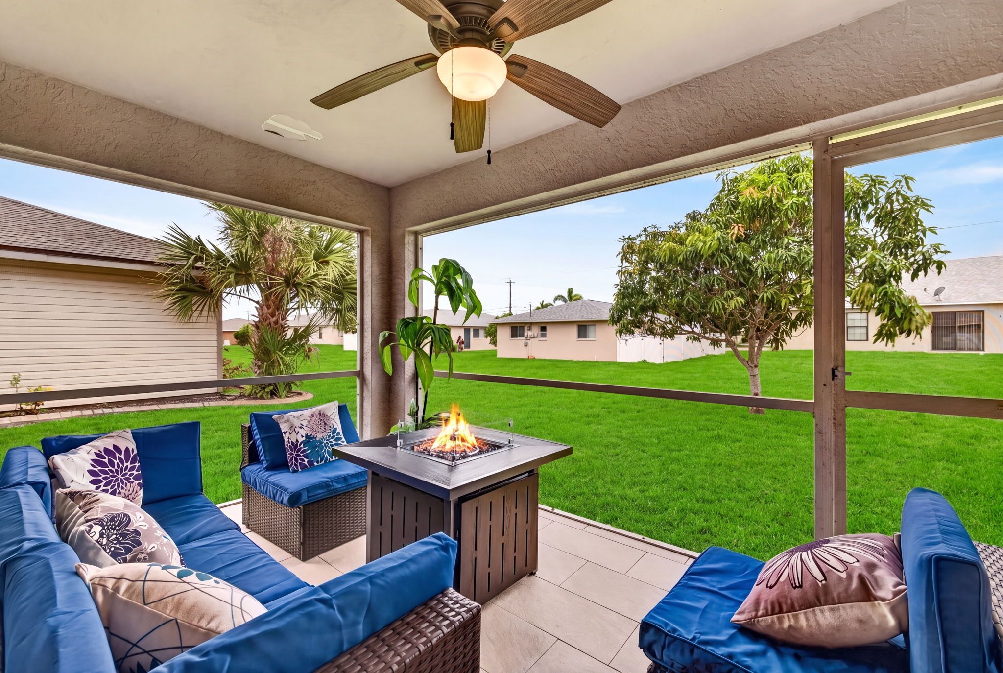 Un patio couvert avec un foyer, du mobilier d’extérieur et une vue sur une pelouse verdoyante et des maisons.