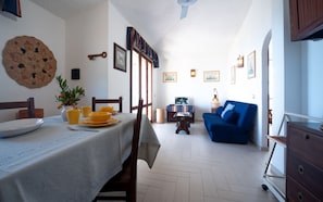 Uma área de refeições com uma mesa posta para quatro pessoas, um sofá azul e uma pequena mesa com abajur.