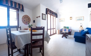 Uma área de refeições com uma mesa posta para dois, um sofá azul e uma televisão ao fundo.