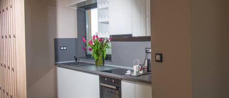 Una cocina moderna con armarios blancos, horno empotrado, pileta y ventana con persianas.