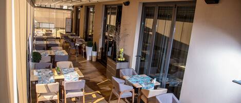 A restaurant with multiple tables and chairs, a wooden floor, and large windows.