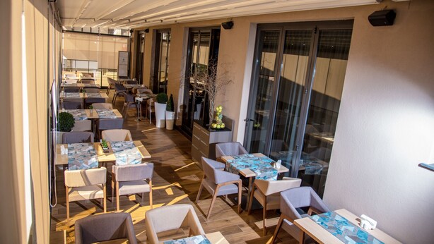 A restaurant with multiple tables and chairs, a wooden floor, and large windows.