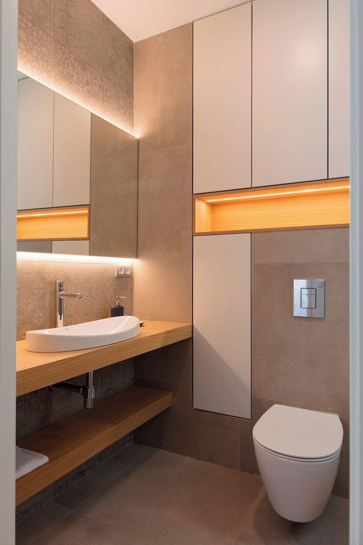 Un baño moderno con un espejo grande, un lavabo blanco, un inodoro y estantes de madera.