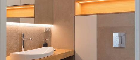 Un baño moderno con un espejo grande, un lavabo blanco, un inodoro y estantes de madera.