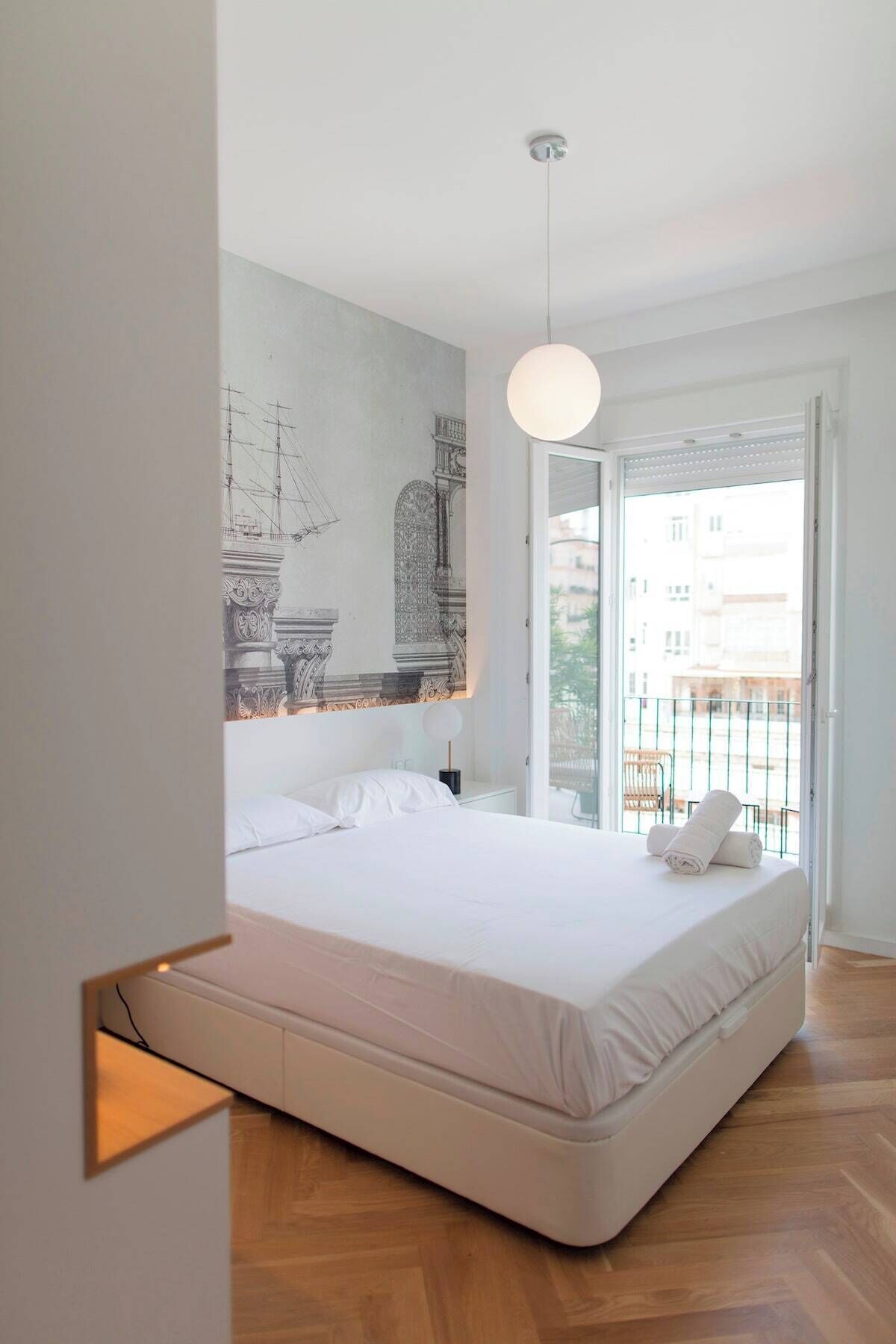 Un dormitorio moderno con una cama grande, una lámpara de techo y vistas a la ciudad desde un balcón.