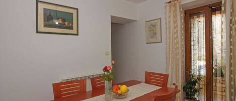 A dining area with a wooden table, chairs, a vase with flowers, and a bowl of fruit.