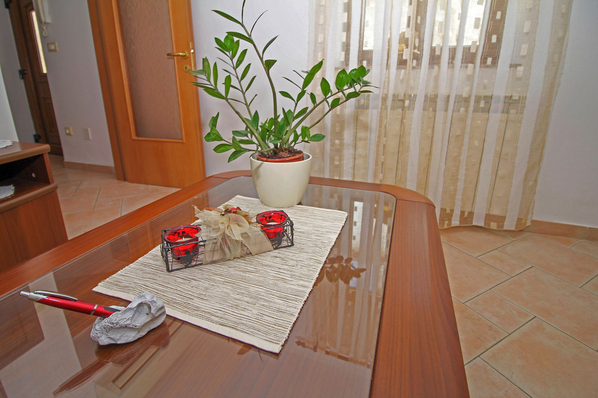A wooden table with a potted plant, a decorative mat, and a red pen.
