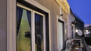 Ein modernes Gebäude mit großen Schiebeglastüren, einer Terrasse mit Holztischen und -stühlen sowie dekorativer Lichterkette.