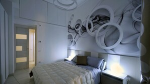 Ein modernes Schlafzimmer mit einem großen Bett, einem Nachttisch und einer Wand mit abstrakten, kreisförmigen Mustern.