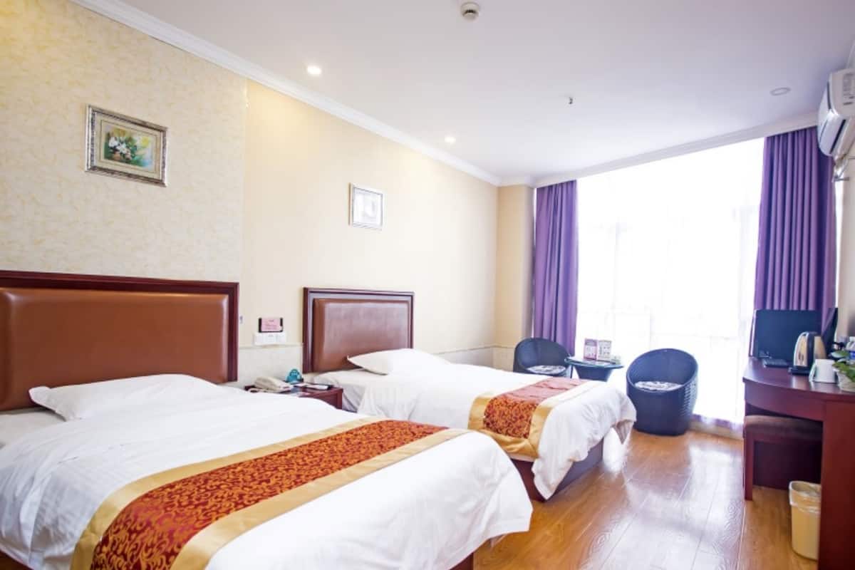 A hotel room with two beds, a desk, a chair, and a window with curtains.