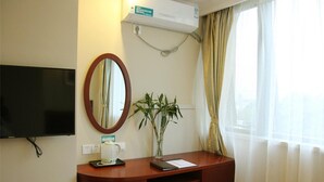 A hotel room with a flat-screen TV mounted on the wall, a wooden desk with a mirror, a potted plant, and a window with curtains. - GreenTree Inn Shanghai Sheshan national tourist resort Express Hotel (Shanghai)