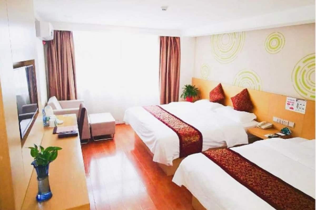 A hotel room with two beds, a desk, a chair, a TV, and a potted plant.
