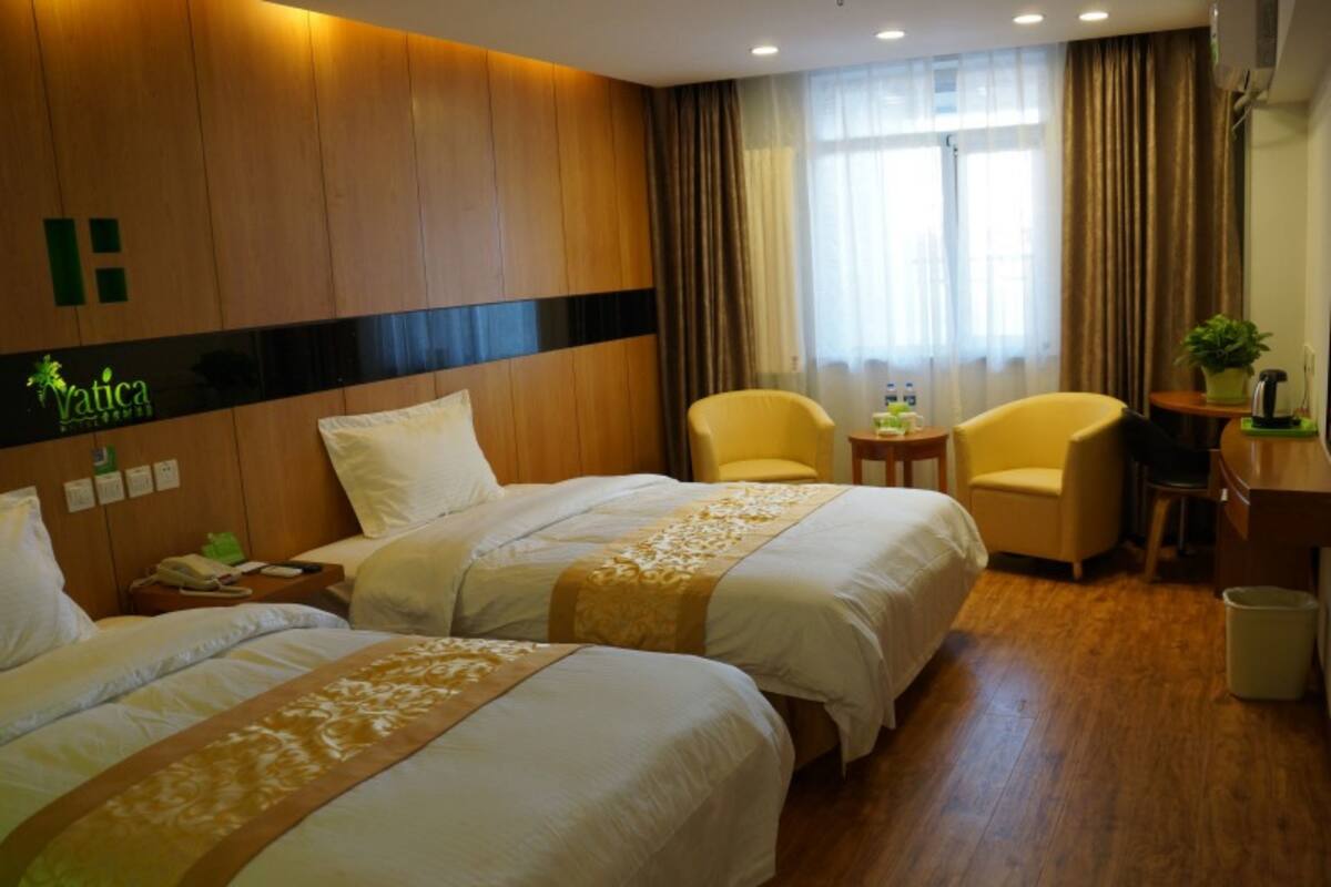 A hotel room with two beds, a desk, a chair, and a small table with a plant.