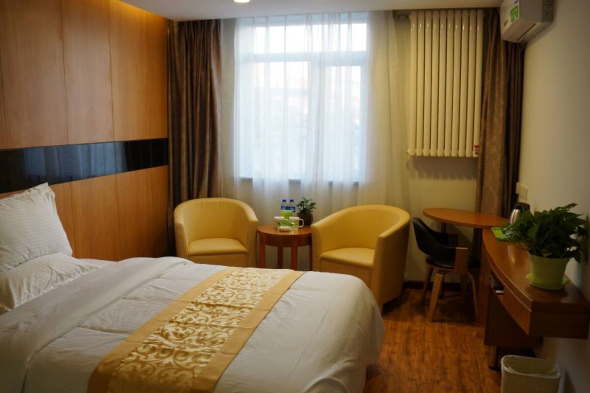 A hotel room with a large bed, two armchairs, a small table with a plant, and a window with curtains.