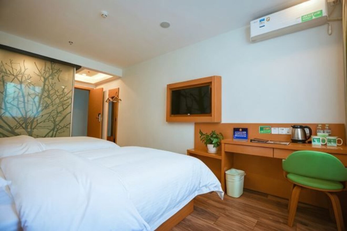 A hotel room with a bed, desk, chair, TV, and a small trash bin.