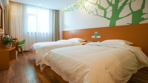 Habitación de hotel con dos camas, piso de madera, un mural en la pared verde y una ventana con cortinas.