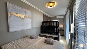 Ein Hotelzimmer mit Bett, Fernseher, einem Gemälde und einem Fenster mit Jalousien.