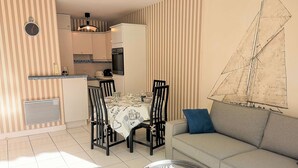 A modern living room with a dining area, a sofa, and a table. There is a kitchen in the background with a refrigerator, stove, and microwave. - Arcachon – One-bedroom flat with sea views in a quiet location (ARCACHON)