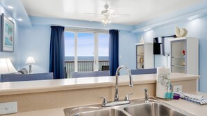 A modern kitchen with a double sink, a ceiling fan, and a view of the sea through large windows.