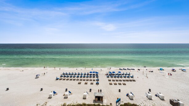 A beach with rows of sun loungers and umbrellas, a lifeguard tower, and the ocean in the background.