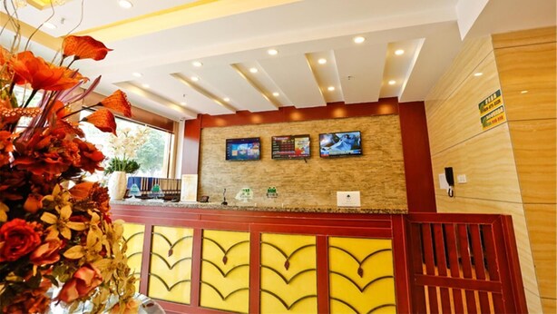 A hotel reception area with a modern design, featuring a reception desk, a large floral arrangement, and a wall-mounted television.