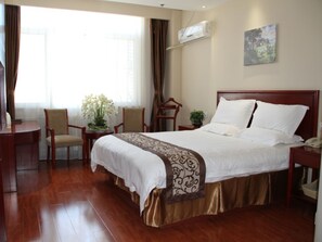 A hotel room with a large bed, a desk, and a chair. There is a window with curtains, an air conditioning unit, and a painting on the wall. - GreenTree Inn Tianjin Jinghai District Jinqiao International Trade Center Express Hotel (Tianjin)