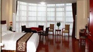 A hotel room with a large bed, a desk, two chairs, a small table, and a large window with curtains.