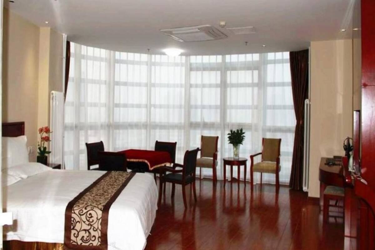 Ein Hotelzimmer mit einem großen Bett, einem Schreibtisch, zwei Stühlen, einem kleinen Tisch und einem großen Fenster mit Vorhängen.