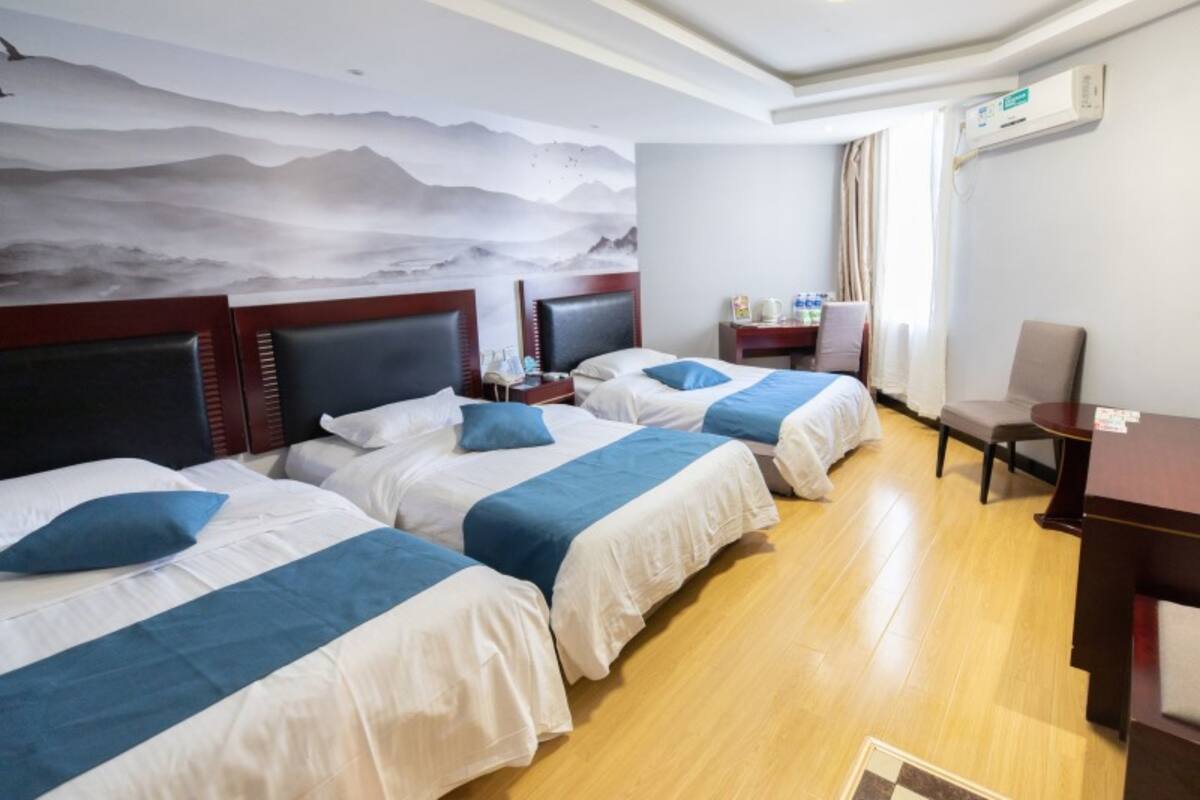A hotel room with two beds, a desk, a chair, and a wall with a mountain mural.