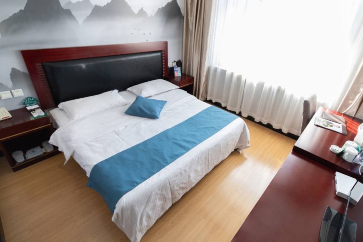 A hotel room with a bed, a nightstand, a desk, and a wall with a mountain design.